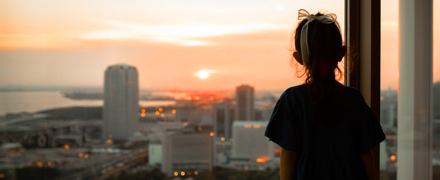 A girl gazes out a window, admiring the vibrant colors of the sunset.