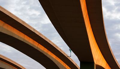 Aerial view of curved concrete highway overpasses bathed in warm golden light against a cloudy sky.