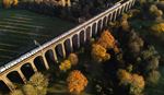 Train on a historic arched viaduct amid fall foliage, aerial view