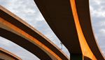 Aerial view of curved concrete highway overpasses bathed in warm golden light against a cloudy sky.